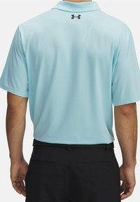Polo de manga corta azul claro con una tela texturizada, con un logotipo de la marca negro en la parte posterior y combinado con pantalones negros.