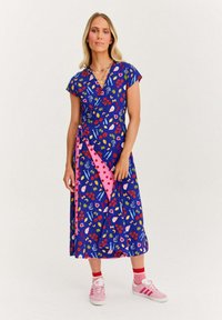 Modré šaty s květinovými a abstraktními vzory, krátké rukávy a růžovým páskem s puntíky. Stylizováno s růžovými teniskami a červenými ponožkami.