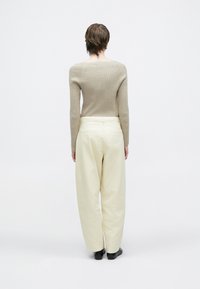 Bež pulover z rebrastim pletenjem, kombiniran z visokim pasom, širokimi kremasto belimi hlačami. Gladek material z minimalističnim dizajnom.