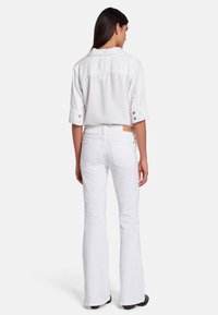 Hvid denimskjorte med opsmøgede ærmer og trykknapper, parret med hvide flagrende jeans med baglommer og et brunt lædermærke.