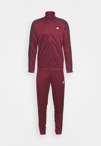 Survêtement bordeaux Adidas avec veste zippée intégrale et pantalon assorti, avec des bandes noires sur les manches et les jambes et des logos Adidas blancs sur la poitrine et la jambe.