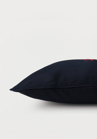 Ορθογώνιο μαξιλάρι σε ναυτικό μπλε με διακριτική κόκκινη κεντητική, εμφανιζόμενο σε κοντινό πλάνο από το πλάι πάνω σε απλό ανοιχτό φόντο.