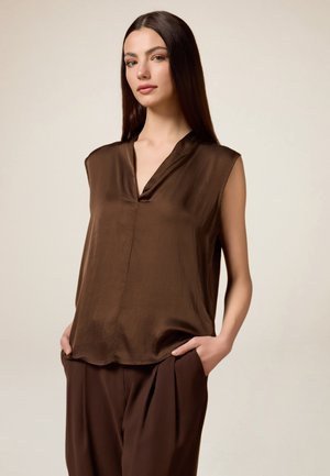 Braun ärmellose Bluse mit V-Ausschnitt, glatter Textur und subtiler Schattierung. Kombiniert mit passenden braunen Hosen, die beide eine lässige Passform aufweisen.