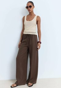 Débardeur en tricot beige clair associé à un pantalon large marron, avec taille élastique et coupe décontractée. Les accessoires comprennent des lunettes de soleil et un bracelet.