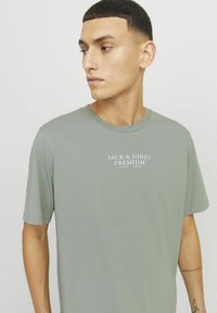 Šviesiai žalia trumpa rankovė T-shirt su apvaliu kaklu, centre krūtinėje esantis baltas tekstas "JACK & JONES PREMIUM". Sklandus paviršius.