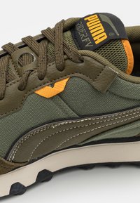 Olivengrøn sneaker med tekstureret overdel, sort sål, orange accenter og mesh-stof. Har fremtrædende snørebånd og mærketag.