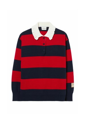 Mujer con un suéter de rayas rojas y azul marino con cuello blanco, pantalones beige de pierna ancha, sudadera amarilla atada a la cintura y zapatos marrones.