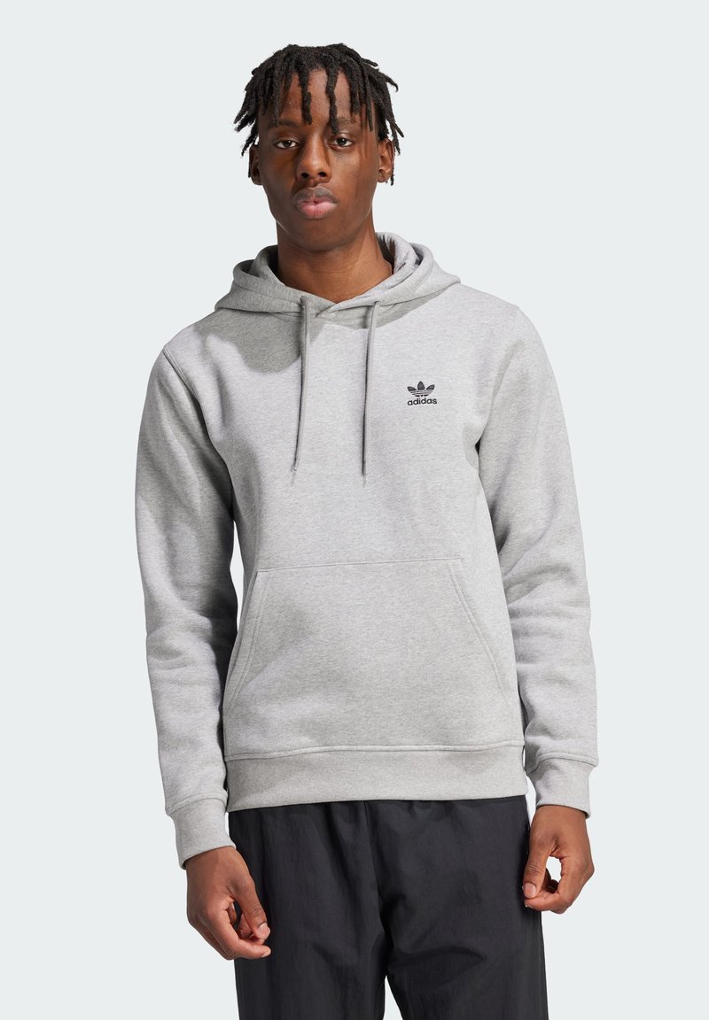 Pilkos spalvos užtrauktukas su kengūros kišene, su raišteliu reguliuojama kapuce ir juodu Adidas logotipu ant krūtinės. Audinys atrodo minkštas ir glotnus.