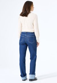 Lichte beige gebreide trui met geribbelde textuur, gecombineerd met hooggesneden donkergblauwe denim jeans met opgerolde boorden en twee achterzakken.
