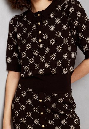 Ensemble haut en tricot marron foncé et jupe avec motif floral losange beige et boutons dorés, porté par une personne aux cheveux bouclés.