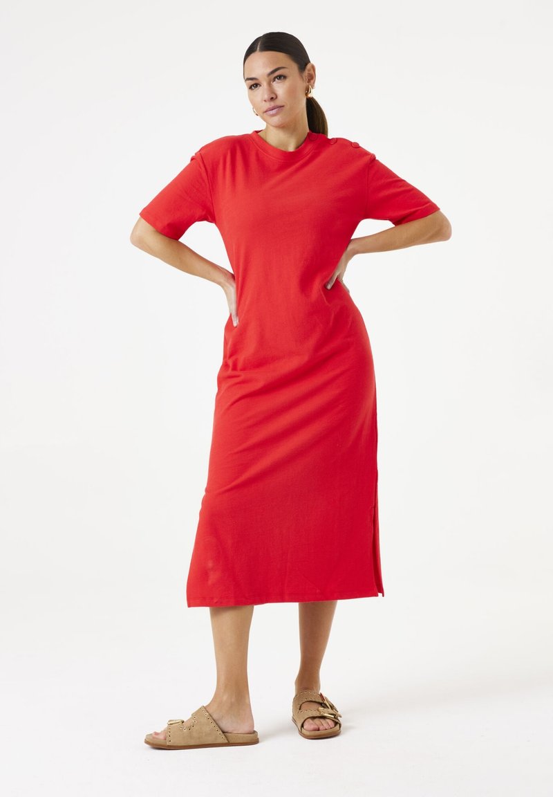 Vestido maxi de algodón rojo con mangas cortas, escote redondo, abertura lateral y botones decorativos en los hombros. Combinado con sandalias planas color marrón.