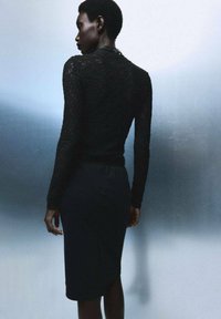 Černý krajkový top s dlouhým rukávem skombinovaný s přiléhavou černou tužkovou sukni. Hladká textura, těsně přiléhající design zvýrazňuje siluetu zezadu.