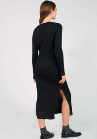 Robe en tricot côtelé noir longue avec des manches longues et une fente sur le côté, présentant une silhouette ajustée et un tissu texturé.
