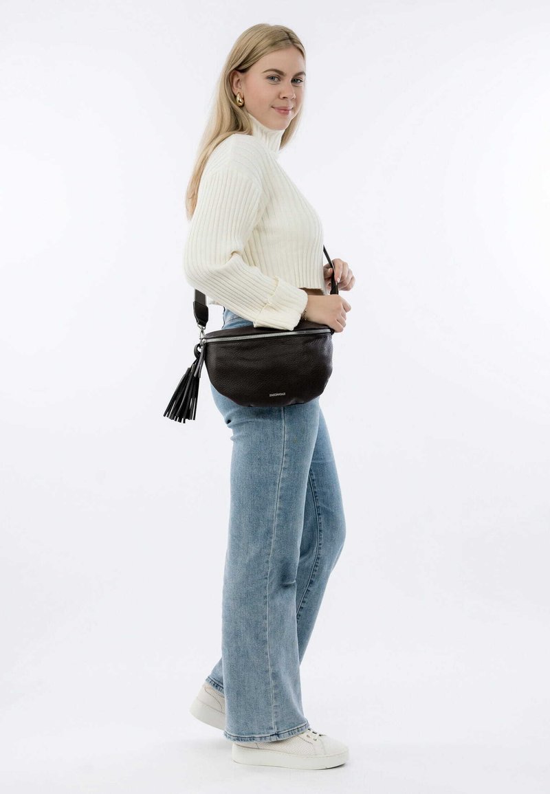 Borsa a tracolla in pelle nera con finitura testurizzata, chiusura con cerniera e decorazione con pon-pon nero. Mostrata con un modello che indossa denim chiaro.