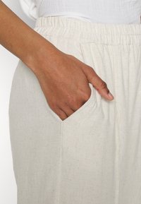 Vita elastiska byxor med midja och en sidoficka. Tyget verkar lätt och texturerat, med subtila fläckar för extra intresse.