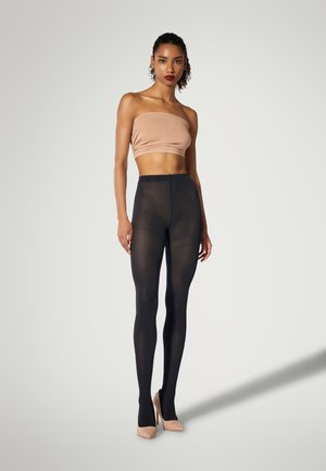 Leggings neri con texture e motivo a rete, abbinati a un top nudo senza spalline e tacchi di colore chiaro. Materiale liscio con un design aderente.
