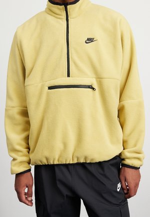 Sudadera de forro polar amarilla con media cremallera negra y logotipo. Cuenta con un bolsillo frontal con cremallera y dobladillo elástico, proporcionando una textura suave.