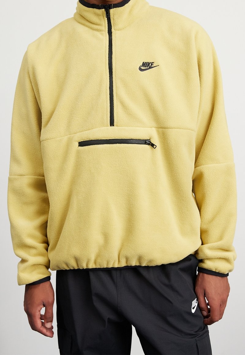 Gul fleece halvdraget tröja med svart dragkedja och logotyp. Har en framficka med dragkedja och elastisk nederkant, vilket ger en mjuk textur.