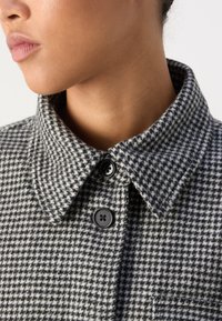 Black and white houndstooth-patterned collar jacket featuring two black buttons, textured fabric, and a chest pocket.