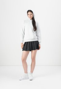 Lys grå hettegenser, svart plisserte skjørt, hvite høye sneakers. Glatte teksturer og uformelt design mot en hvit bakgrunn.