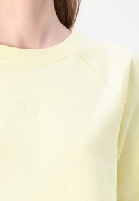 Ανοιχτό κίτρινο φούτερ με ριγέ λαιμόκοψη και ραμμένα μανίκια. Διαθέτει ανάγλυφο λογότυπο στο στήθος και υφασμάτινη υφή.