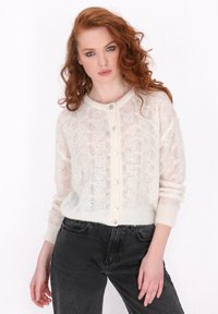 Cardigan leggero a maglia color crema, con un motivo testurizzato e bottoni sul fronte. Abbinato a jeans in denim scuro a vita alta.