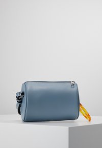 Borsa cilindrica blu in pelle con zip argento, dotata di un manico colorato e trasparente su un lato e di un design minimalista.
