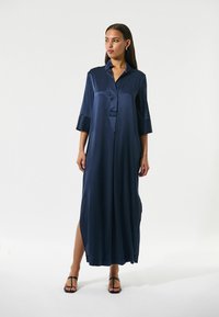 Abito in satin blu navy con scollatura a colletto, maniche a tre quarti e spacco laterale, caratterizzato da una silhouette ampia e allungata.