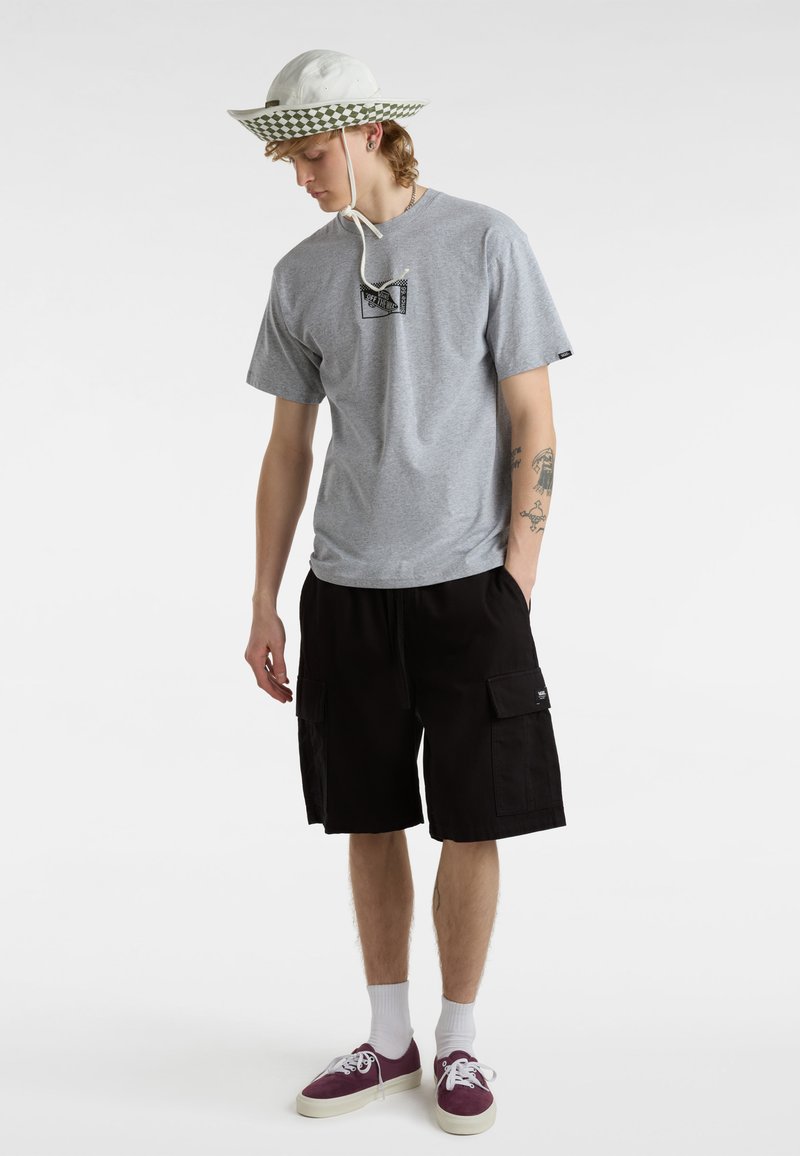 Grijs T-shirt met korte mouwen en een logografiek; zwarte cargoshorts; witte vissershoed met groen geblokt bandje; bordeauxrode sneakers met witte zolen.
