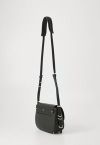 Borsa a tracolla in pelle nera con tracolla regolabile, accessori in tonalità oro e un piccolo logo impresso sulla parte anteriore, su uno sfondo semplice.