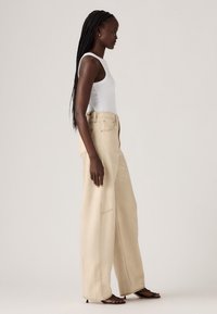 Beige wijde broek met hoge taille, gemaakt van een gestructureerde stof. Inclusief zijzakken en zichtbare stikdetails.
