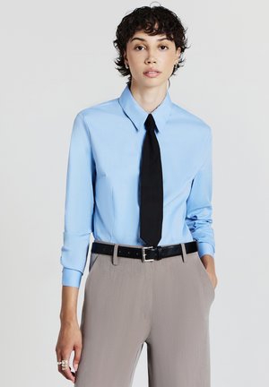 Light blue long-sleeve shirt with a pointed collar, paired with a black tie. Beige trousers with a fitted black belt. Smooth texture.