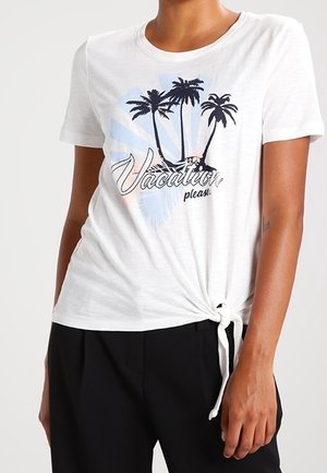 Camiseta blanca de manga corta con diseño de palmera y texto “Vacation please”, anudada al dobladillo, usada con pantalones negros.