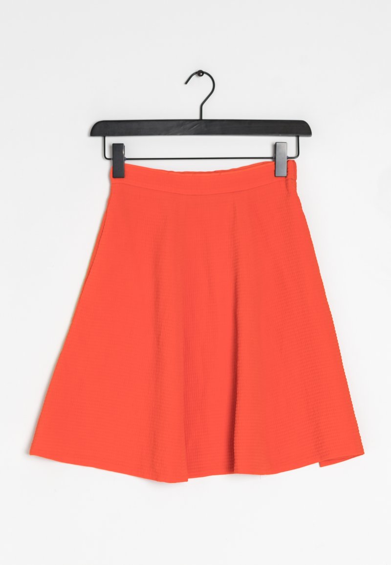 Jupe patineuse orange vif suspendue sur un cintre noir sur un fond blanc uni.