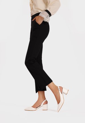 Pantaloni neri a sigaretta con tasche laterali abbinati a décolleté bianche con punta quadrata e tacco chunky. Tessuto liscio, design minimale.