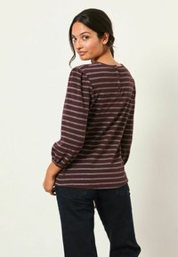 Langärmliges gestreiftes Oberteil in tiefem Kastanienbraun und Silber, mit Puffärmeln und einer Knopfdetail hinten, kombiniert mit dunklen Jeans.