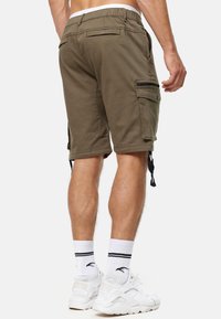 Shorts cargo vert olive avec une taille élastique, des poches latérales et des cordons de serrage au niveau des jambes, fabriqués en coton durable.