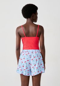 Rode, mouwloze top met een gestructureerde afwerking, gecombineerd met blauwe geblokte shorts met een kersenpatroon. Ontspannen pasvorm, elastische tailleband.