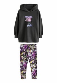 Sweat-shirt à capuche noir à manches longues avec un imprimé graphique, associé à des leggings à motif floral violet avec des accents jaunes et blancs.