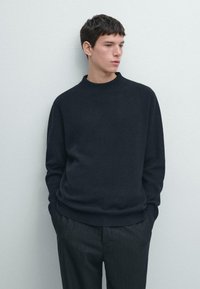 Ciemny prążkowany sweter z dzianiny z okrągłym dekoltem, luźnym krojem i długimi rękawami, zestawiony z spodniami w cienkie paski.