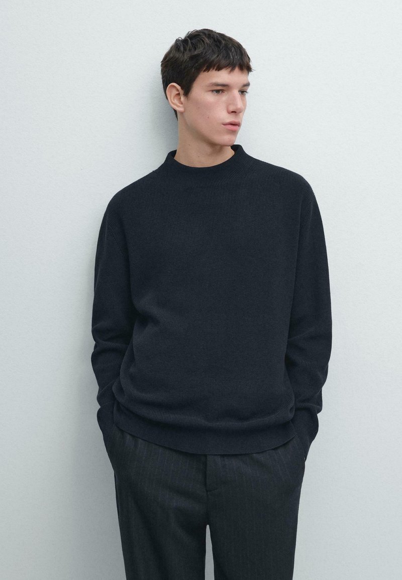 Ciemny prążkowany sweter z dzianiny z okrągłym dekoltem, luźnym krojem i długimi rękawami, zestawiony z spodniami w cienkie paski.