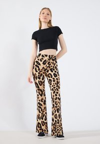 Hlače s leopard uzorkom u nijansama bež i crne, uparene s pripijenim crnim kratkim topom. Mekani materijal s glatkom teksturom.