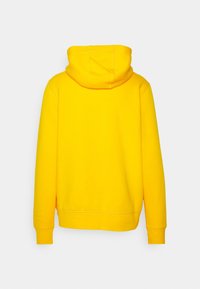 Sudadera con capucha amarilla de textura suave, presenta un bolsillo tipo canguro y puños acanalados. Tela lisa y ajuste relajado. Vista trasera.