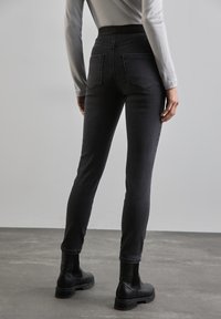 Högmidjade svarta denimjeans med en slät textur, smal passform, två bakfickor och ett brett midjeband. Matchade med svarta ankelstövlar.