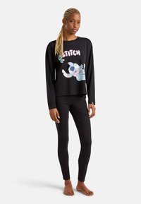 Haut noir à manches longues avec un graphique de dessin animé de Stitch, associé à des leggings noirs, tous fabriqués dans un tissu doux et extensible.