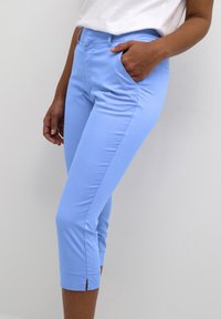 Pantaloni blu chiaro a vita corta realizzati in tessuto morbido, dotati di tasche laterali e orlo con un piccolo spacco su ciascun polsino.
