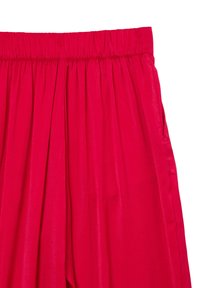 Pantaloni in raso rosso con una cintura elastica ampia e una texture liscia, caratterizzati da morbide pieghe per una maggiore voluminosità.