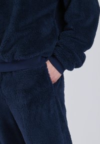 Marineblauer Fleece-Trainingsanzug mit einer strukturierten, weichen Außenseite. Verfügt über gerippte Bündchen und eine Fronttasche an der Hose. Wärmender und gemütlicher Stoff.