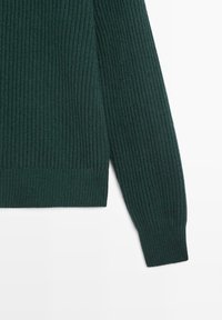 Dunkelgrüner, gerippter Pullover mit strukturierter Strickoptik, langen Ärmeln und geradem Saum. Das Material wirkt weich und warm.