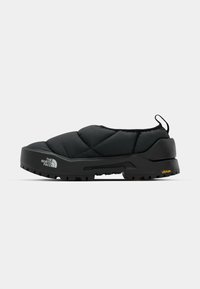 Black quilted slip-on shoe with a robust rubber sole, featuring a textured grip and a logo on the toe. Vibram branding on the heel.